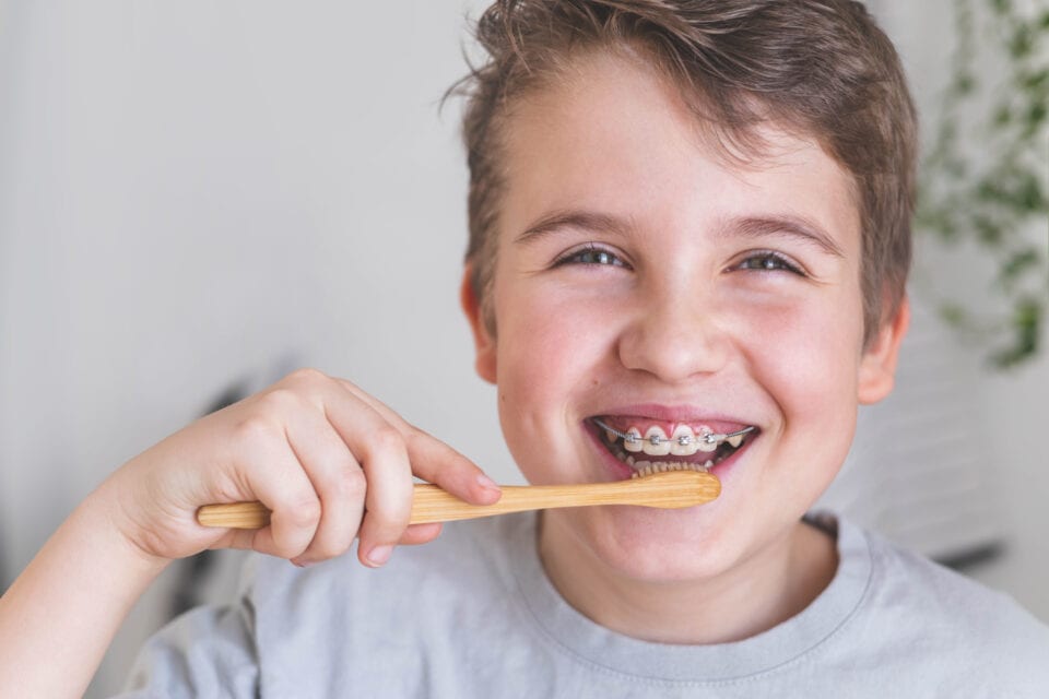Happy boy child cleaning teeth with braces use wooden eco friendly toothbrush healthy lifestyle