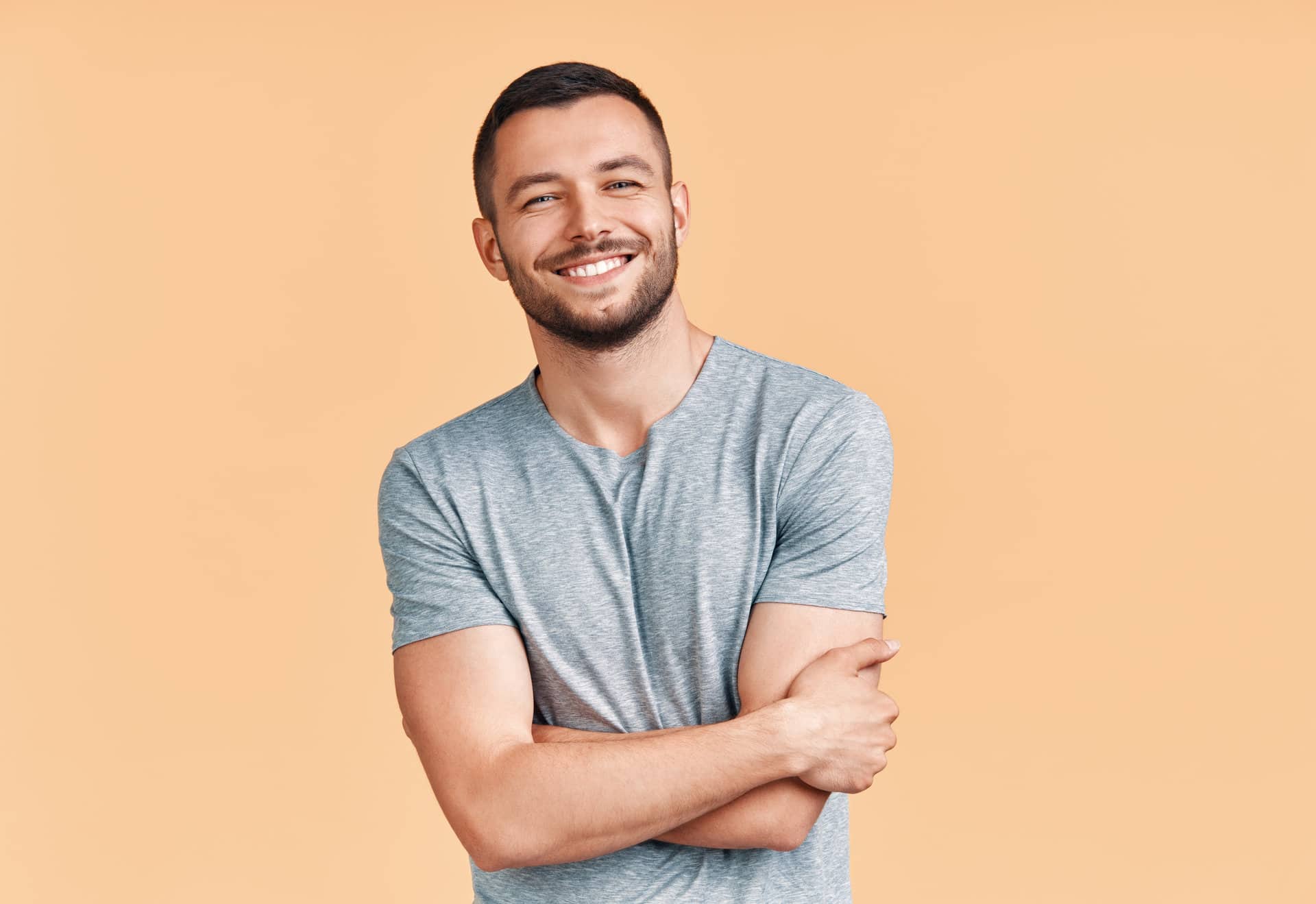 Happy smiling handsome man with crossed arms looking to camera over beige background. Emotions concept